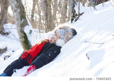 The girl fell into a snowdrift with her back and looked into the frame in a snowy forest The girl fell into a snowdrift with her back and looked into the frame in a snowy forest 74885885