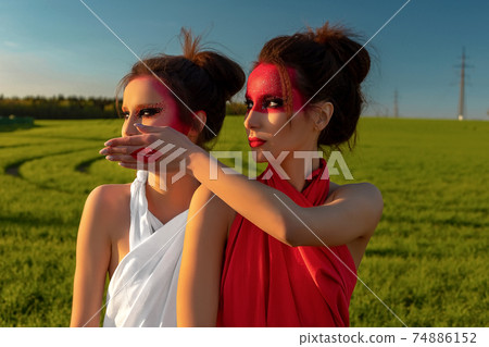 Portrait of two girls, brunettes with creative makeup against the background of a green field and blue sky 74886152