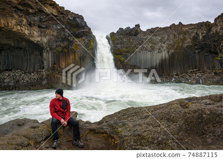 Tourist sits at the Aldeyjarfoss waterfall in northern Iceland Tourist sits at the Aldeyjarfoss waterfall in northern Iceland 74887115
