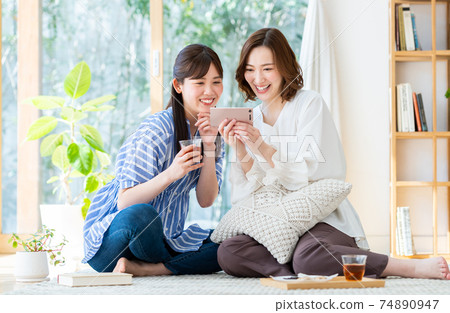 一個年輕的女人，看著她的智能手機上的視頻 74890947