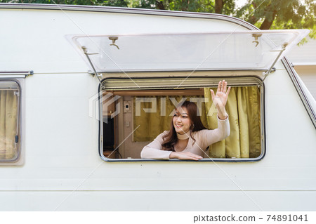 happy woman raising her hand at window of a camper RV van motorhome 74891041