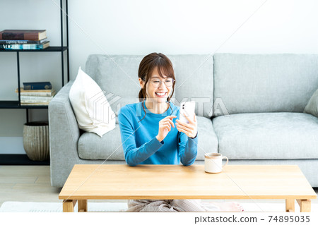 A woman with glasses using a smartphone in the living room A woman with glasses using a smartphone in the living room 74895035
