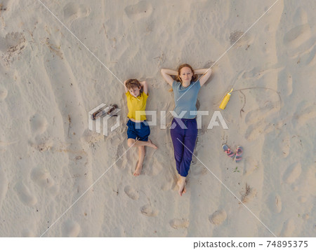 Mom and son are lying on the sand at sunset. View from the drone. Paradise, travel, vacation concept Mom and son are lying on the sand at sunset. View from the drone. Paradise, travel, vacation concept 74895375