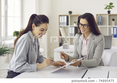 Woman signs a lease or purchase agreement given to her by a bank manager or real estate agent. 74895475