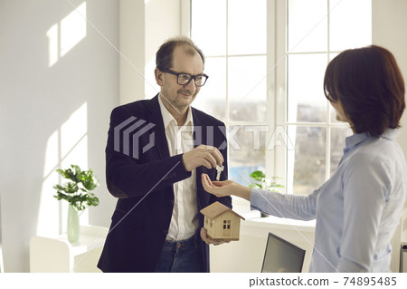 Smiling middle-aged real estate agent gives key to new house to his happy client Smiling middle-aged real estate agent gives key to new house to his happy client 74895485
