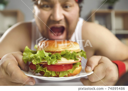 Funny man who failed his diet enjoying fast food and eating big delicious burger Funny man who failed his diet enjoying fast food and eating big delicious burger 74895486