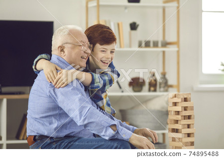 Happy little grandson embracing his grandfather while playing fun games together Happy little grandson embracing his grandfather while playing fun games together 74895488