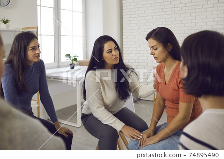 Women in support group comforting and helping young woman who's suffered from emotional abuse 74895490