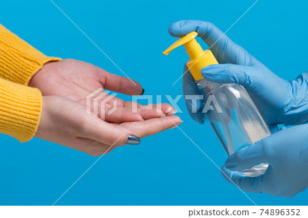 concept of protection against viruses and bacteria, hands are treated with a disinfectant, on a blue background concept of protection against viruses and bacteria, hands are treated with a disinfectant, on a blue background 74896352