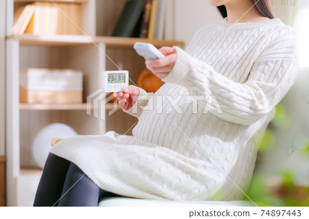 看著溫濕度計並通過遙控器操作的孕婦 看著溫濕度計並通過遙控器操作的孕婦 74897443