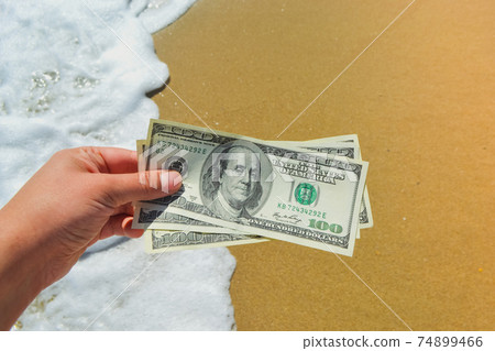 Girl holding a money bill of 300 dollars on background of sea waves Girl holding a money bill of 300 dollars on background of sea waves 74899466