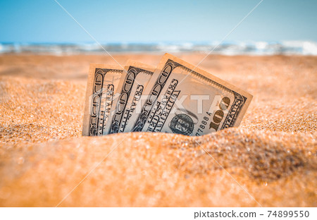 Money dolars half covered with sand lie on on sandy beach near sea ocean 74899550