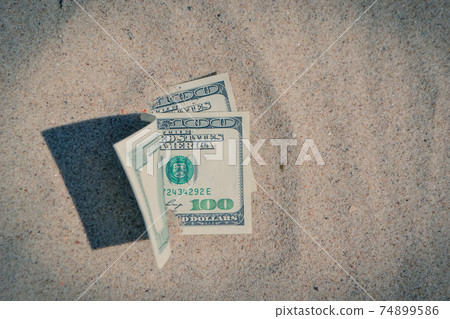Money dolars half covered with sand lie on beach close-up 74899586