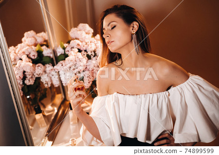 A young woman in an evening dress with perfume stands in front of the home dressing table.The girl uses perfume before going to a party. 74899599
