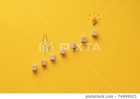 Silhouette of a businessman walking up the stairs towards a light bulb 74899925