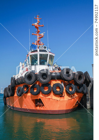 Tug boat with  bright orange hull is moored in a port 74902117