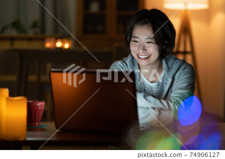 Young woman looking at a computer in the living room at night 74906127