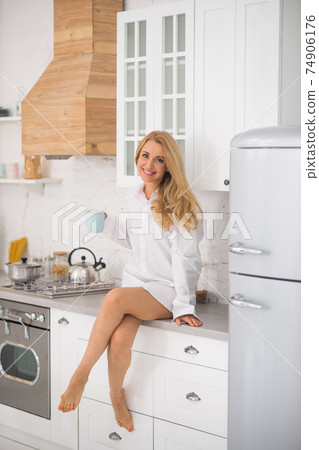 Joyful woman with cup sitting in kitchen 74906176