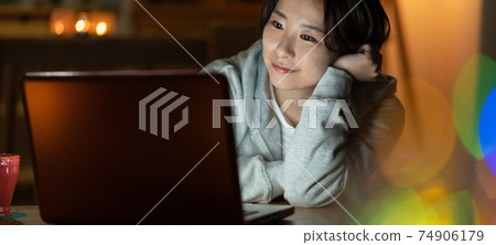 看一台計算機在客廳裡的年輕女子在晚上橫幅大小 74906179