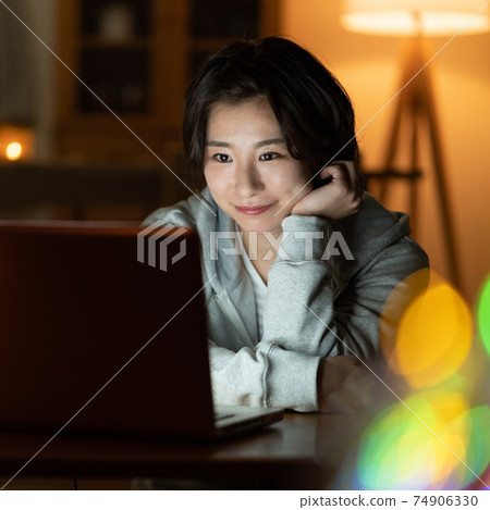 看一台計算機在客廳在夜間廣場的年輕女子 74906330