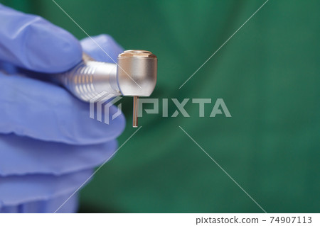 Dentist's hand in glove with dental handpiece. Dentist's hand in glove with dental handpiece. 74907113