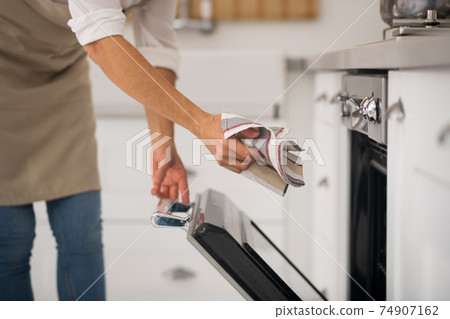 Housewife in apron opening the oven in the kitchen 74907162