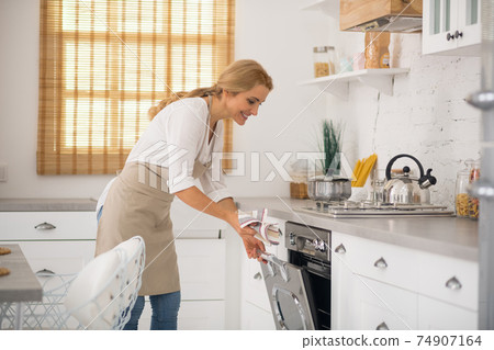Housewife in apron opening the oven in the kitchen Housewife in apron opening the oven in the kitchen 74907164