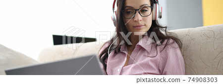 Woman in headphones with clipboard in her hands sits on couch with laptop Woman in headphones with clipboard in her hands sits on couch with laptop 74908303