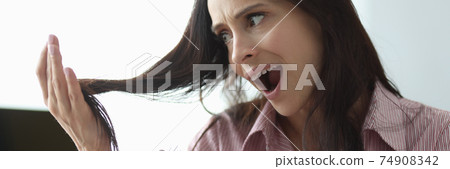 Woman holds comb in her hand and looks at her hair in panic. 74908342