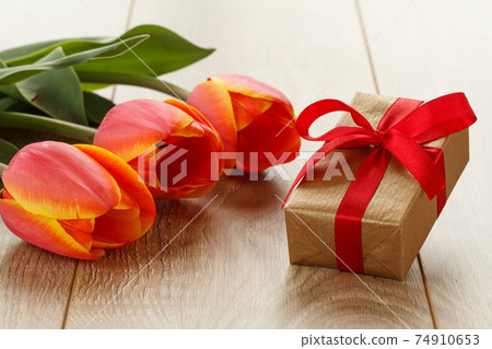 Gift box with red ribbon and flowers on wooden boards. 74910653