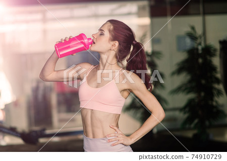 Young female at the gym trainer holding a bottle of water 74910729