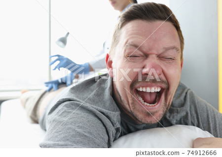 Man lying on couch with his mouth open. Nurse giving injection in buttock 74912666