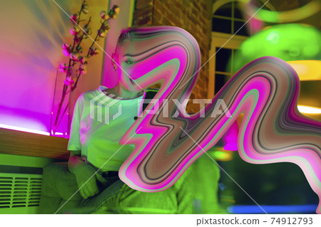 Cinematic portrait of stylish woman in neon lighted interior using a smartphone. The face is smeared, sucked into the phone. The concept of social network dependency 74912793