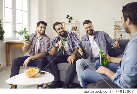 Group of happy friends sitting on sofa, drinking beer, sharing funny stories and laughing 74912807