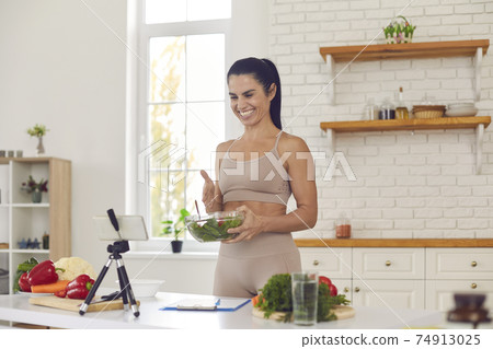 Cheerful fit vlogger filming culinary video, giving dieting tips and sharing healthy salad recipe 74913025