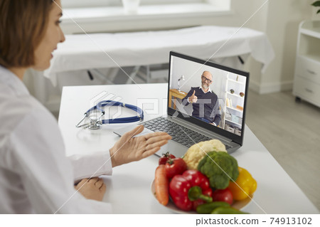 Online doctor sitting at desk with laptop and video calling happy senior patient 74913102