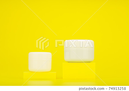 Two unbranded cosmetic jars on yellow podiums against bright yellow background with copy space 74913258