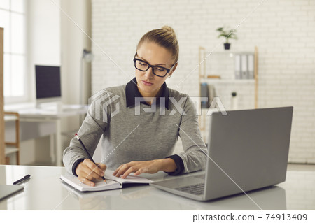 Focused woman taking online course, watching webinar and writing in her notebook 74913409