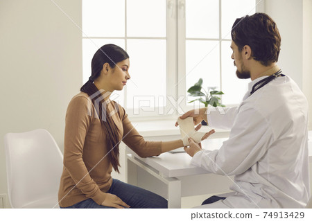 Professional doctor at the hospital wrapping young woman's injured wrist with bandage Professional doctor at the hospital wrapping young woman's injured wrist with bandage 74913429