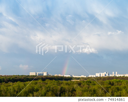 blue rainy clouds and rainbow over city in spring 74914861
