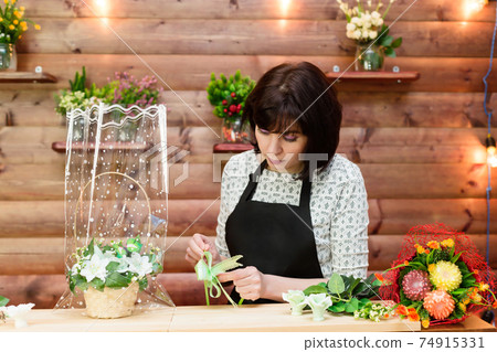 Brunette florist of flower business wraps flowers in plastic 74915331