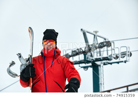 Male snowboarder in a red suit walking on the snowy hill with snowboard, Skiing and snowboarding concept 74915359
