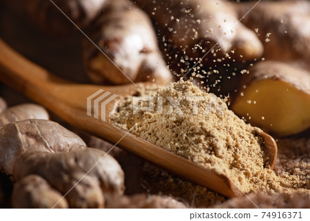 Fresh ginger root and ground ginger powder pours into wooden spoon 74916371