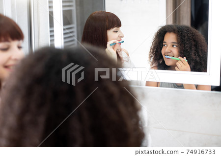 Mother and daughter having fun while cleaning teeth together. Joyful smiling positive mommy and her daughter doing morning oral hygiene routine Mother and daughter having fun while cleaning teeth together. Joyful smiling positive mommy and her daughter doing morning oral hygiene routine 74916733