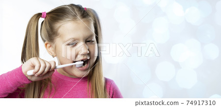 Preschool girl with first adult incisors and a toothbrush. The milk tooth has fallen out, and a permanent tooth grows in the open mouth. Dental hygiene concept 74917310