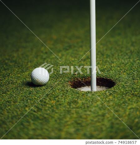 golf ball nearby hole with pin flag, green grass background, closeup view 74918657