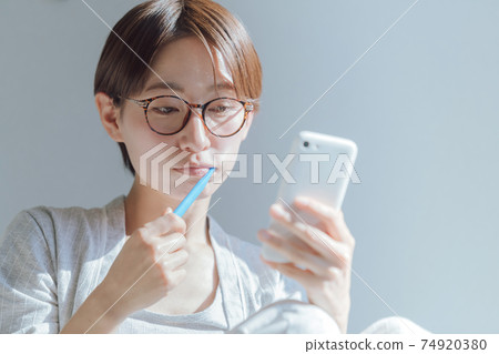 Lifestyle image of a woman looking at a smartphone while brushing her teeth in the morning Lifestyle image of a woman looking at a smartphone while brushing her teeth in the morning 74920380