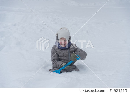 The girl is digging the snow. The child plays with a lot of snow. A rosy child in the cold. Nice walk and play 74921315