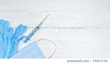 syringe for injections, nitrile gloves and a medical mask on light wooden table 74925116