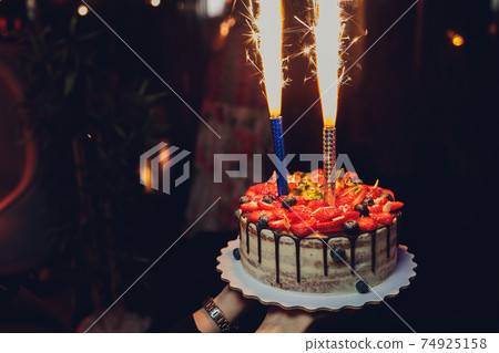 Birthday cake with candles. Candles on cake. Cake for holiday. Beautiful white cake with strawberries on dark background. Vertical photo. 74925158